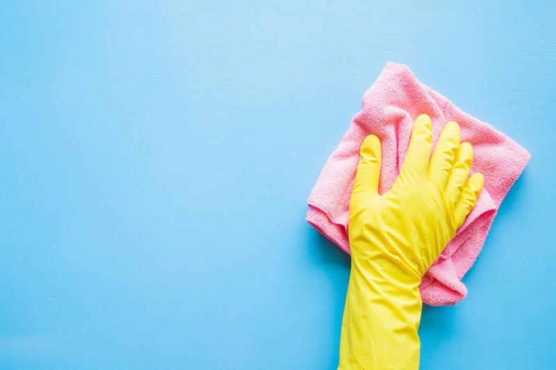 Does An AC Kill Mold? Hand in a yellow rubber glove, wiping a blue wall with a pink rag.