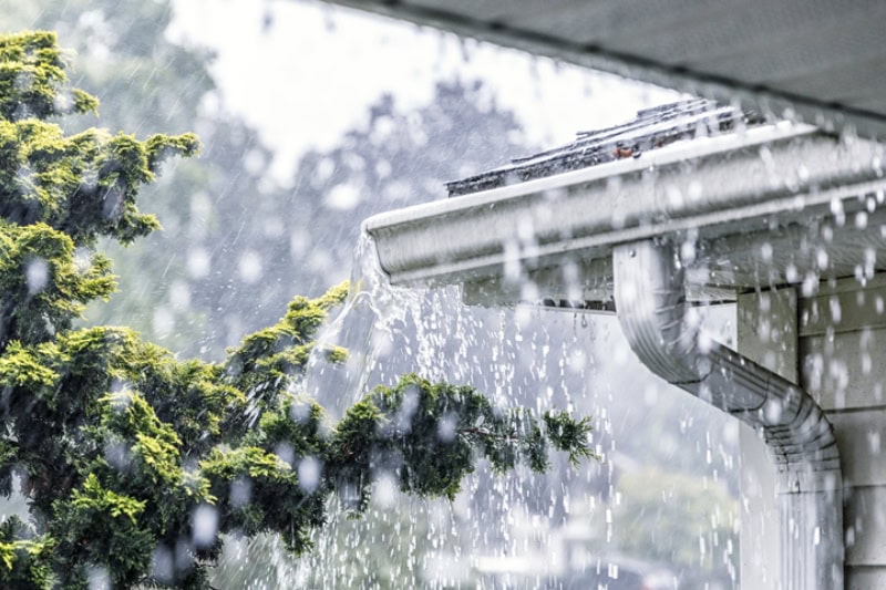 Drenching downpour rain storm water is overflowing off the tile shingle roof.