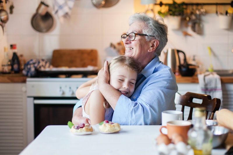 Why Do I Need a Humidifier in the Fall? Grandmother hugging young granddaughter in an autumn decorated kitchen.